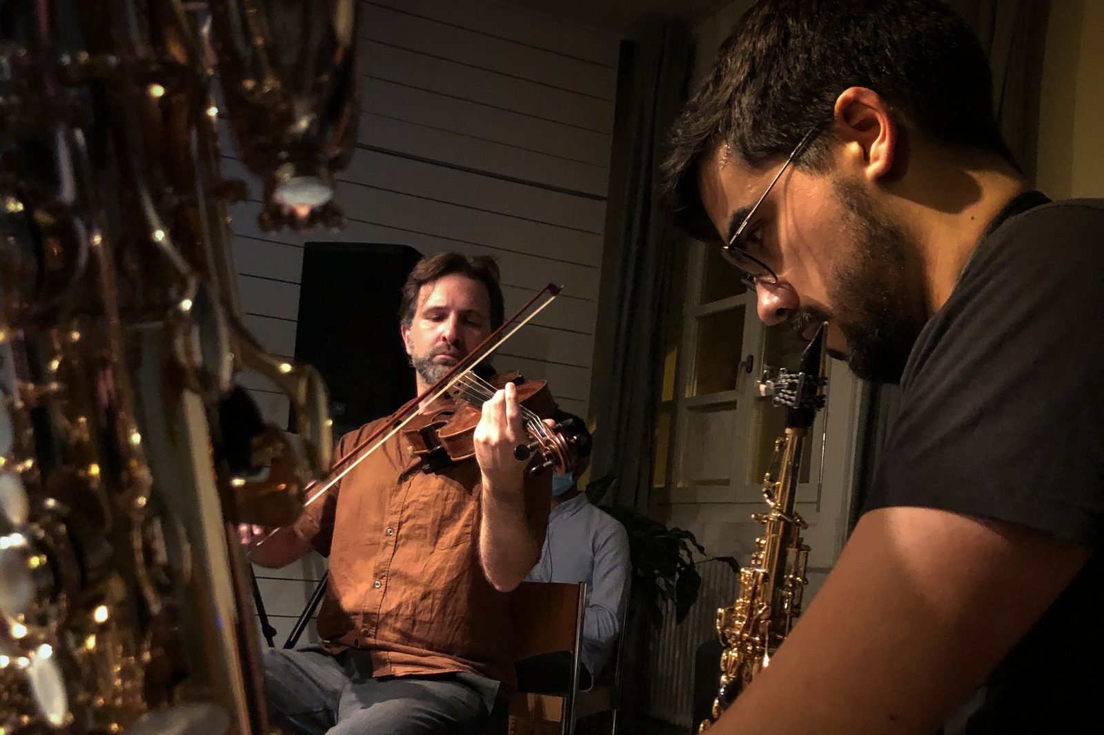 Diego Kohn playing the violin in concert, with a saxophone in the foreground