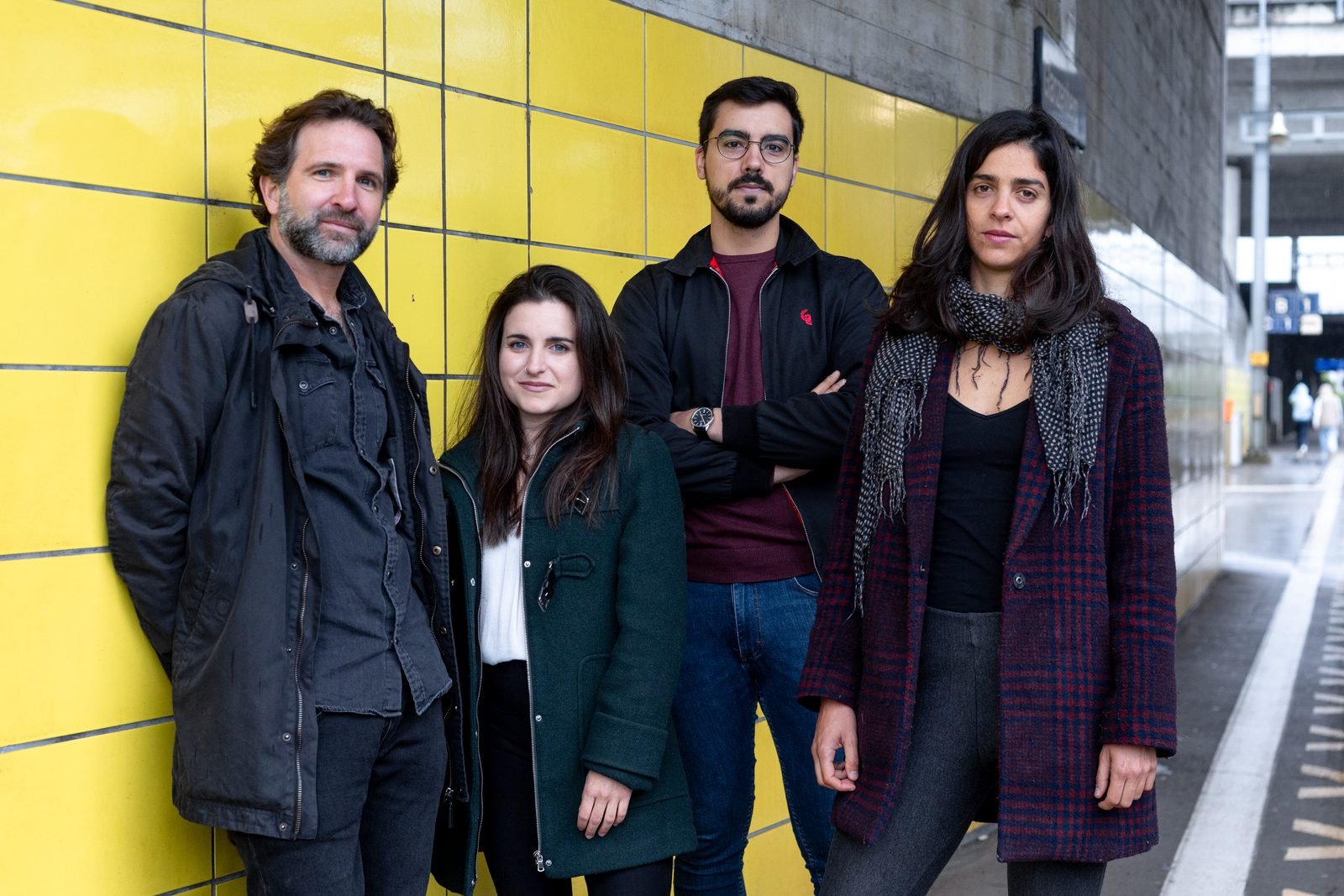 The four members of Slide Ensemble standing against a yellow tiled wall in a railway station