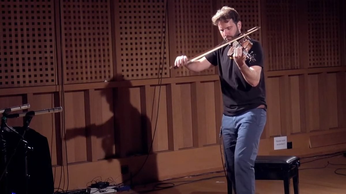 Diego Kohn playing violin solo, his shadow on the wooden wall