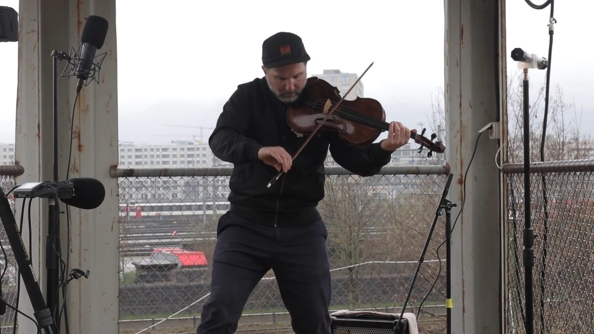 Side view of Diego Kohn bowing the viola, railway tracks behind him