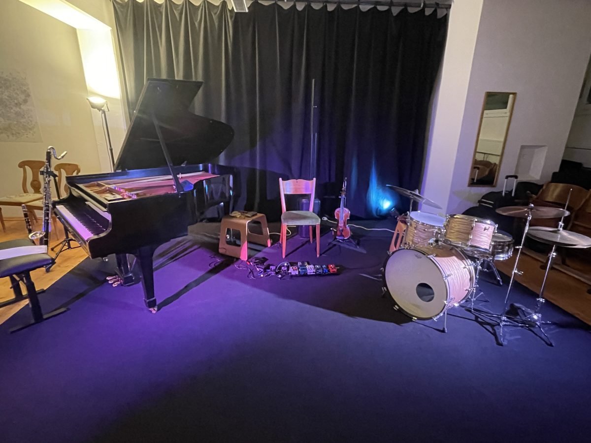 The stage before the concert: grand piano, chair with viola, pedals and drum kit in blue light