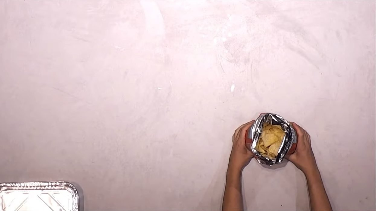 Seen from above: two hands open a bag of crisps next to an empty aluminium tray