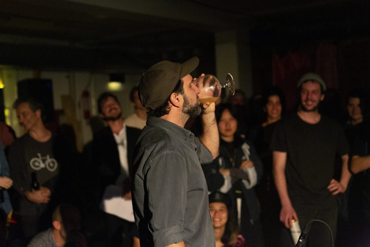 Diego Kohn drinking from a glass in the middle of a standing audience