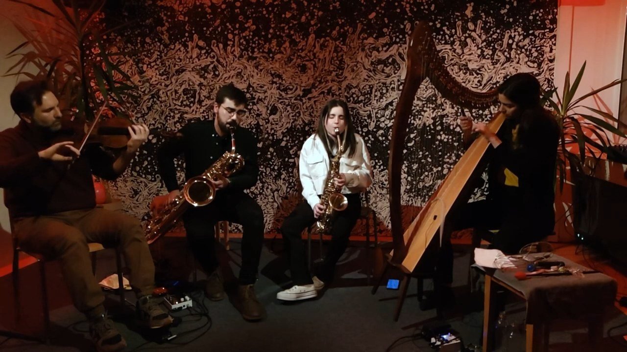 Slide Ensemble in concert at the Schönegg Varieté: viola, baritone saxophone, soprano saxophone and harp in front of a dark patterned wall