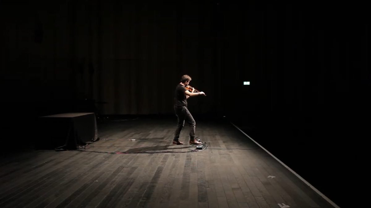 Diego Kohn playing violin alone on a dark stage in a pool of light