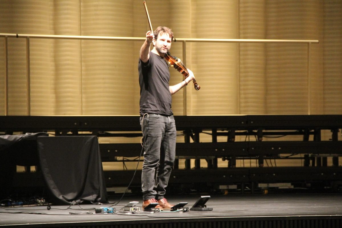 Diego Kohn on stage raising his bow, pedals at his feet
