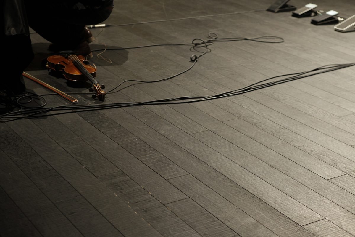 The violin and bow on the stage floor among cables and volume pedals